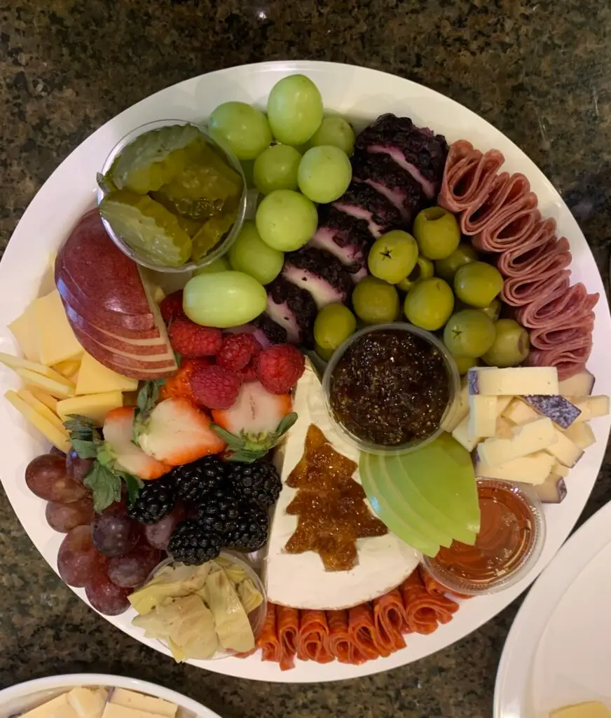 charcuterie board with grapes, ham, cheese in the shape of a christmas tree, strawberries, and apples